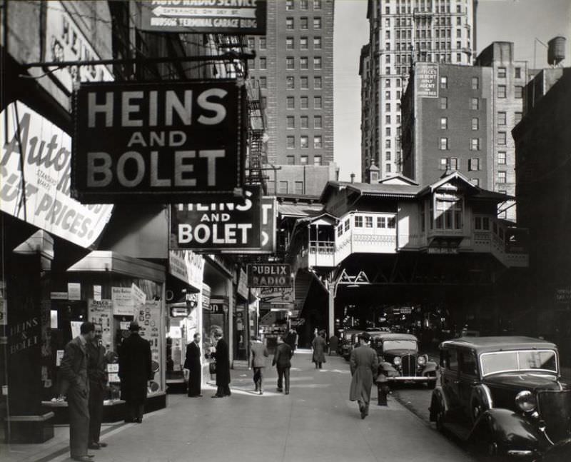 Radio Row, Cortlandt Street, Manhattan. Men window shop in store selling radios, elevated railroad station, Ninth Avenue line, right center, subway entrance visible.