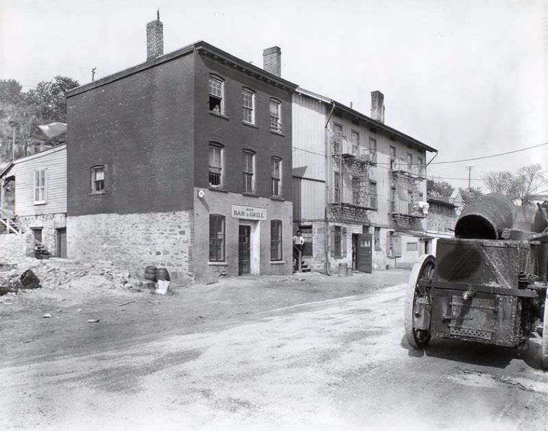 Ewen Avenue No. 2565 (Bar and grill), Spuyten Duyvil, Bronx. Bar and grill and other buildings built into hillside along street, man looks on from steps, girl from window above, vehicle with barrels, right.