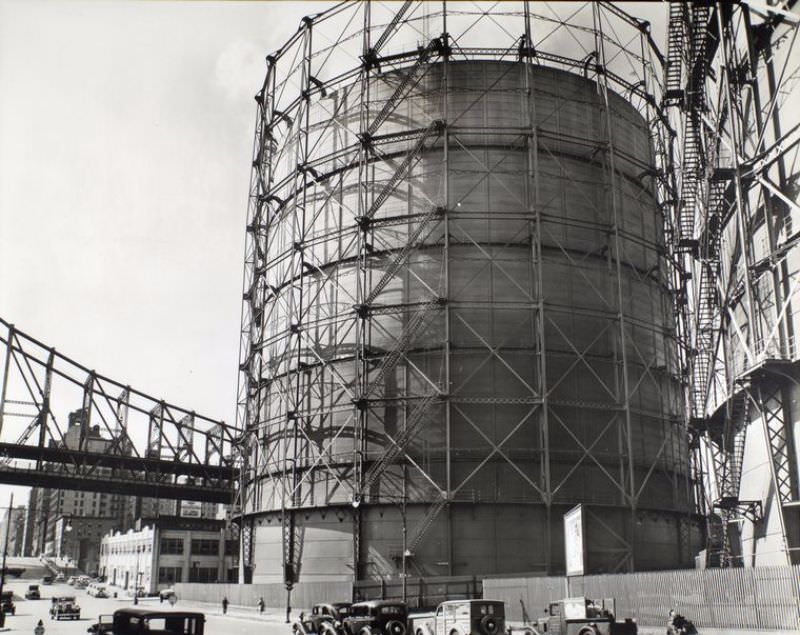 Gas tank and Queensboro Bridge, East 62nd Street & York Avenue, Manhattan. Huge gas tanks dwarf Queensboro Bridge (left) and cars on street below.