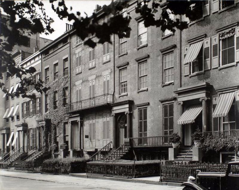 Washington Square North, nos. 121-125, Manhattan. Row of brick houses, all with pairs of columns at door, ones at ends have awnings; house for rent is shuttered; Jaguar car partially visible.