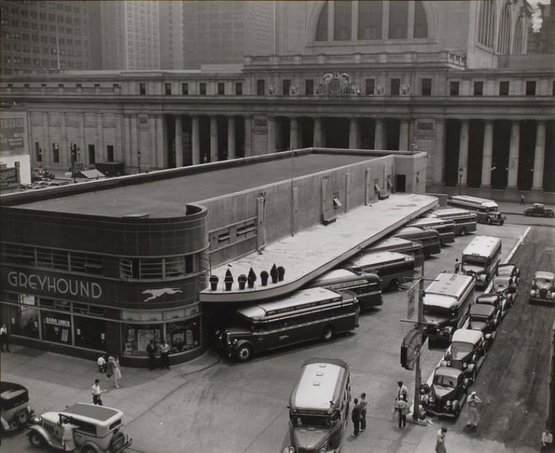 Greyhound Bus Terminal, 33rd and 34th Streets between Seventh and Eighth Avenues, Manhattan. View of the terminal from above, showing buses, two story station with curved corners; cabs in foreground, Penn station beyond.