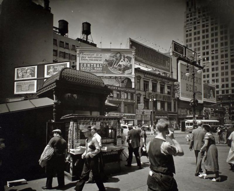 Union Square, 14th Street and Broadway, Manhattan. Men and women hurry past newstand outside uptown subway entrance, street beyond is lined with businesses topped with large billboards.