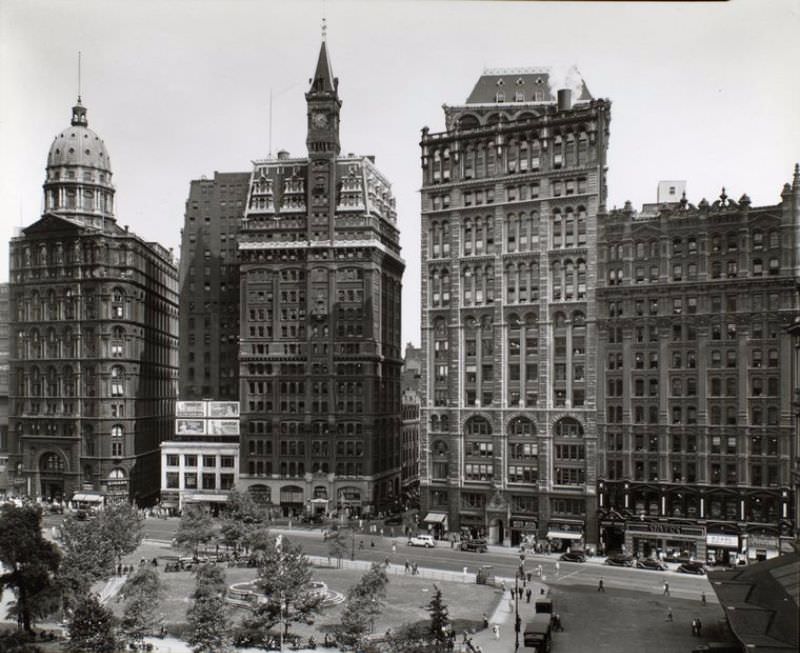 Looking across City Hall Park at buildings lining Park Row, including the Tribune and Pulitzer buildings and the statue of Franklin.