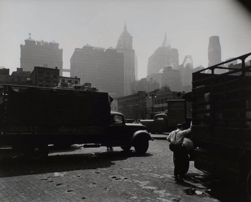 City Vista, West Street, looking east, Manhattan. Men and trucks in foreground, Hudson Terminal and other buildings in the haze beyond.