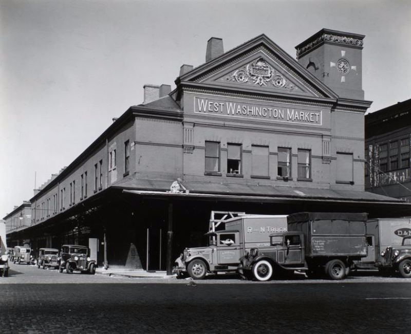 West Washington Market, Washington Street and Loew Avenue, Manhattan.Man works on roof of market's porch, trucks out front, cars along side street, signs for butchers.