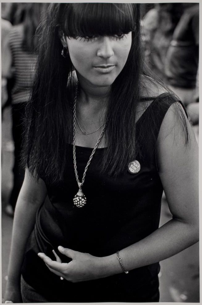 Woman in black with necklace and button.