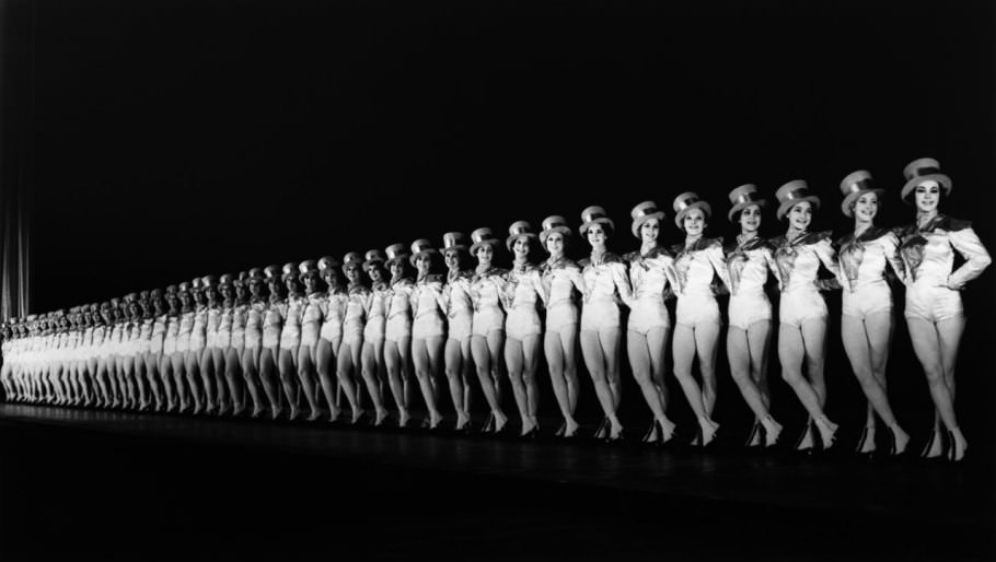 Onstage in 1937, the Rockettes cut a sharp, diagonally receding line—in white and top hats—against the dark backdrop. Originally just one line of dancers, the Rockettes today encompass two 40-girl casts.