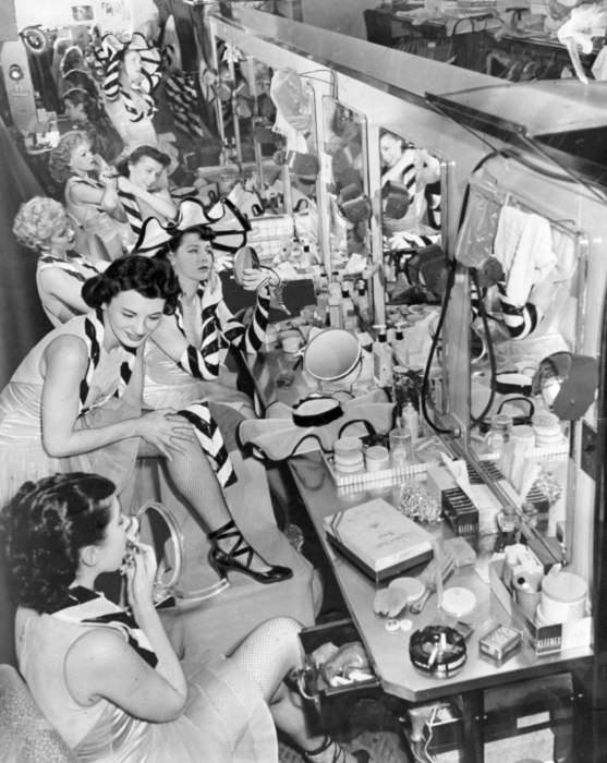 Backstage at the vanity area in 1952, the Rockettes set their makeup with powder, adjust their stockings, and stick in their final bobby pins before going onstage.