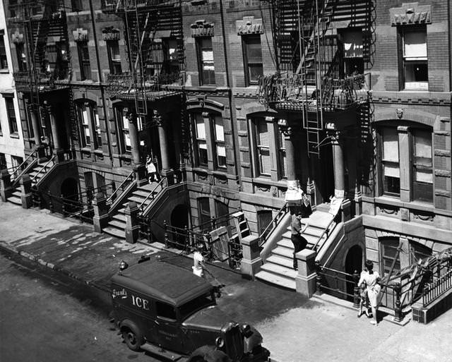 A street scene in Greenwich Village, New York, with a woman hosing down the pavement next to an ice-delivery van, 1950.