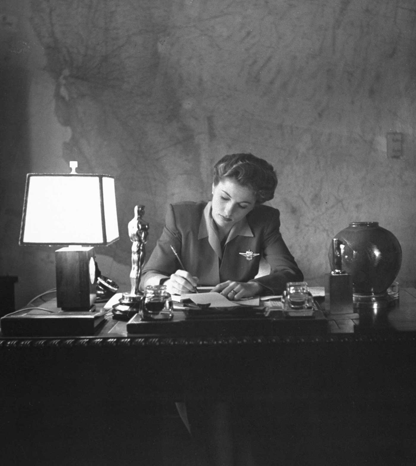 Joan Fontaine doing the household bookkeeping next to the Oscar she won for her role in Hitchcok's Suspicion, 1942.