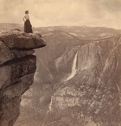 A female tourist stands on the edge of Overhanging rock, nearly a mile straight down and only a step–from Glacier Point (N.W.) across valley to Yosemite Falls, Yosemite, Cal., circa 1902.